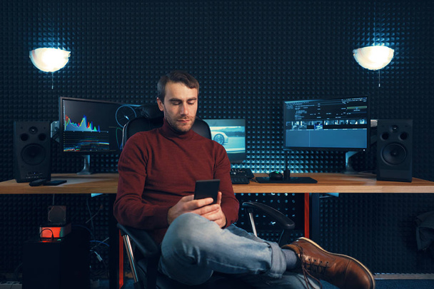 Nuori mies työskentelee studiossa älypuhelimen ja tietokoneen avulla
. - Valokuva, kuva