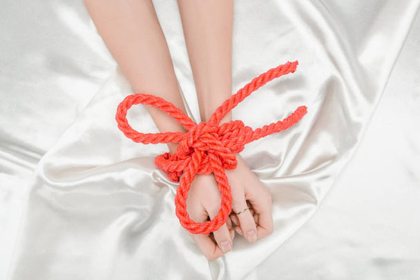 cropped view of female hands bounded with bright red rope on satin cloth - Fotografie, Obrázek