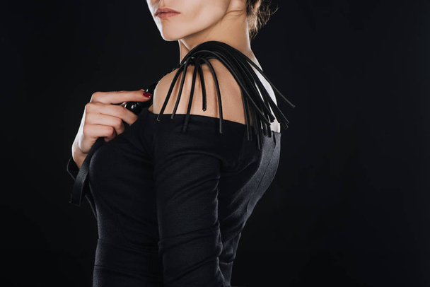 вид сбоку женщины, держащей кожаную порку плетью, изолированную на черном
 - Фото, изображение