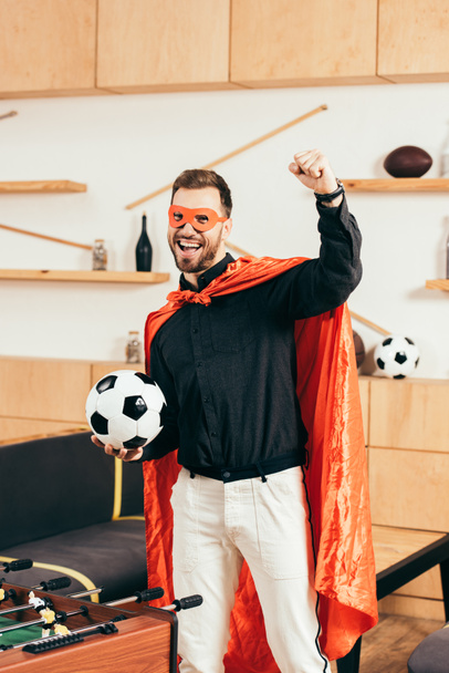 happy young man in red superhero costume with soccer ball gesturing in cafe - Fotoğraf, Görsel