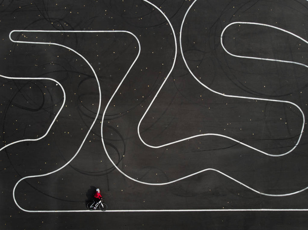 Vista aérea de una mujer montando una bicicleta en un estacionamiento. Zigzag líneas de pista en el asfalto
. - Foto, imagen