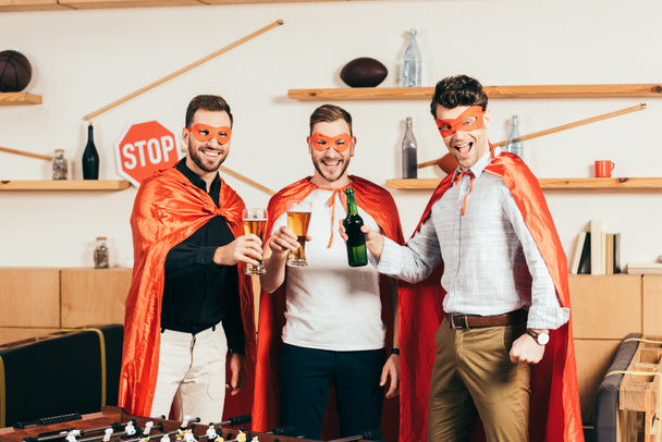 portrait of happy young men in superhero costumes clinking drinks in cafe - Photo, Image