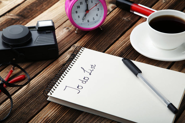 To do list in notepad with cup of coffee, alarm clock and retro camera on wooden table - 写真・画像
