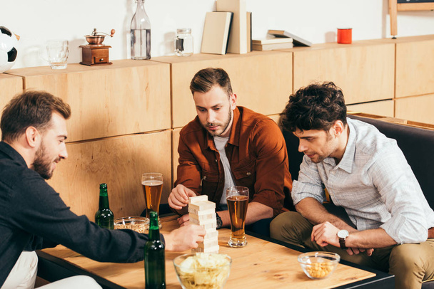 focused friends playing blocks wood game at tabletop with snacks and beer  in cafe - Photo, Image