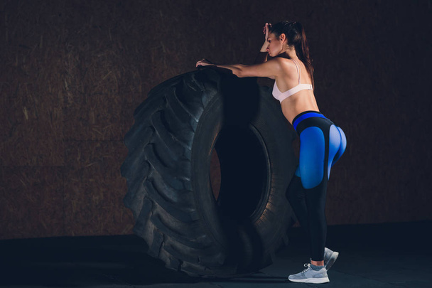 Fitness woman flipping wheel tire in gym. Fit female athlete working out with a huge tire. Back view. Sportswoman doing an strength exercise training. - Valokuva, kuva