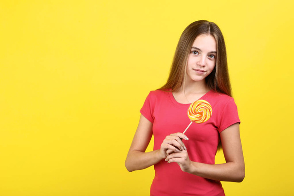 Young girl with lollipop on yellow background - Фото, зображення
