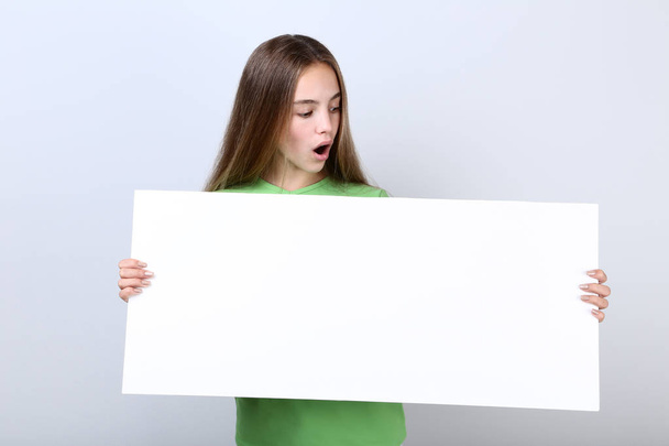 Surprised young girl holding blank board on grey background - Fotoğraf, Görsel