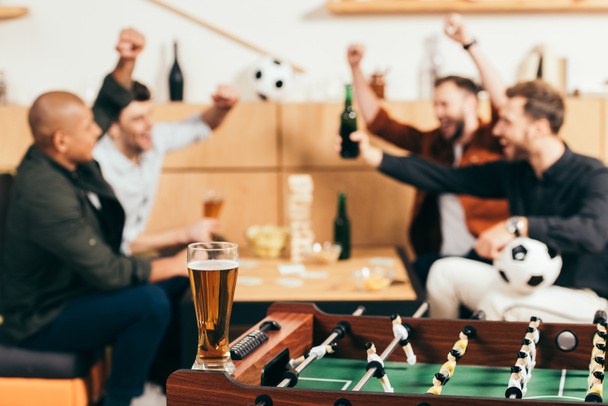 enfoque selectivo de amigos multiculturales felices haciendo gestos mientras se sienta en la mesa con cerveza y aperitivos en la cafetería
 - Foto, Imagen