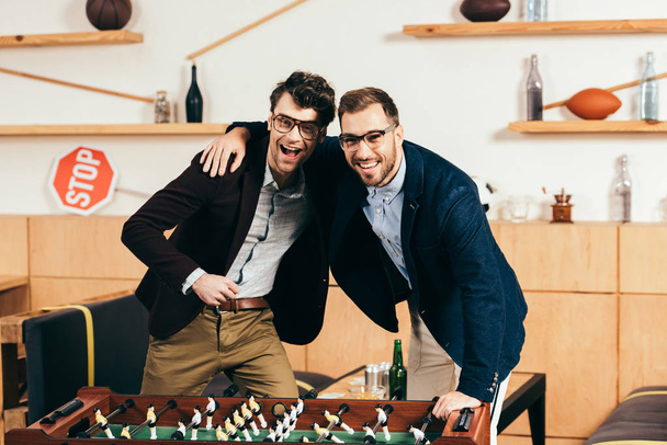 portrait of smiling businessmen with beer standing at table soccer in cafe - Photo, Image