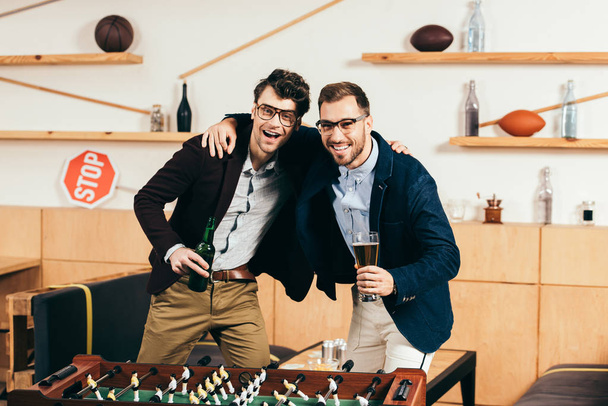 portrait of smiling businessmen with beer standing at table soccer in cafe - Photo, Image