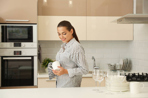 Young woman wiping clean cup in kitchen. Dish washing - Photo, image