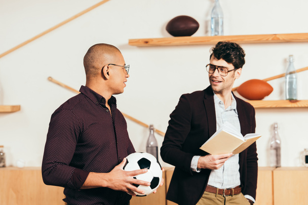 portrait of multiethnic businessmen with soccer ball and book in cafe - Photo, Image