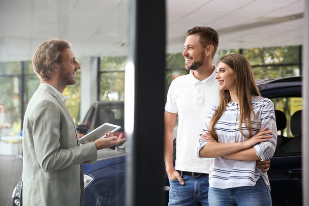 Salesman with tablet consulting young couple in car dealership - Foto, afbeelding