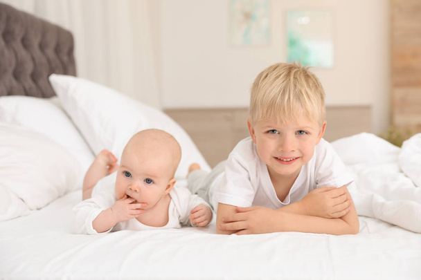 Cute boy with his little sister lying on bed at home - Fotó, kép