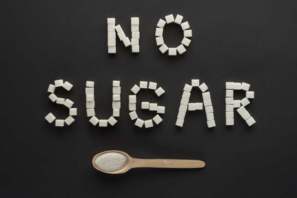 flat lay of "no sugar" lettering made of cubes with wooden spoon isolated on black  - Photo, Image