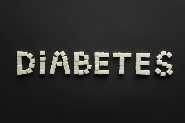 top view of "diabetes" lettering made of sugar cubes on black - Photo, Image