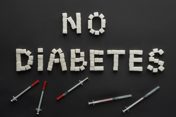 "no diabetes" lettering made of sugar cubes with insulin syringes on black - Fotografie, Obrázek