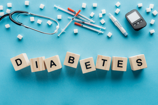 "diabetes"letters gemaakt van houten blokjes met medische apparatuur op blauwe achtergrond - Foto, afbeelding