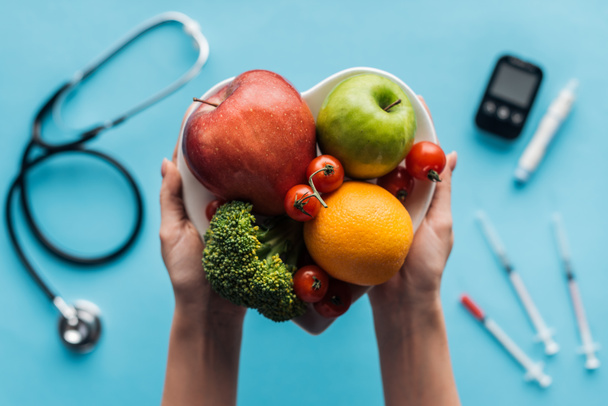 frutas y verduras en manos femeninas con equipo médico sobre fondo azul
 - Foto, Imagen
