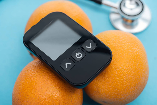 close up view of glucometer on oranges with stethoscope on blue background - Foto, Imagen