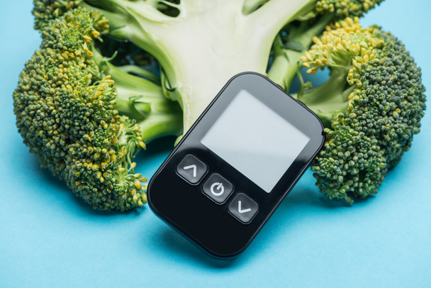 Close-up van glucometer met broccoli op blauwe achtergrond - Foto, afbeelding