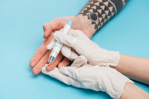 oříznutý pohled ženy v rukavicích testování hladina glukózy s injekční stříkačkou na modrém pozadí - Fotografie, Obrázek
