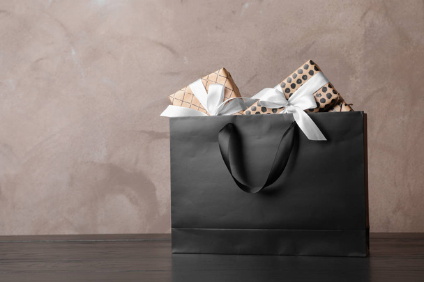 Einkaufstasche aus Papier mit Henkeln voller Geschenkboxen auf dem Tisch. Mock up für Design - Foto, Bild