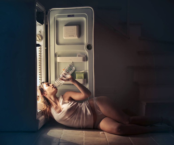 молодая женщина освежает себя водой в холодильнике
 - Фото, изображение