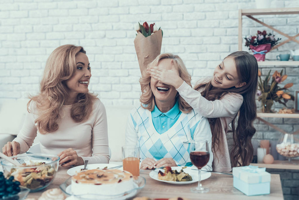 Family Preparing Surprize for Grandmother at Home. Cake on Table. Happy Family. Mother with Daughter. Smiling Women. Smiling Grandmother. Celebration Concept. Glass of Wine. Closed Eyes. - Fotografie, Obrázek