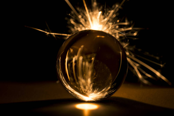 Burning sparkler behind a glass ball on a black background. - Fotoğraf, Görsel