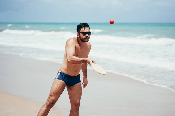 Young Brazilian man playing beach tennis on the beach with swimwear - Fotoğraf, Görsel
