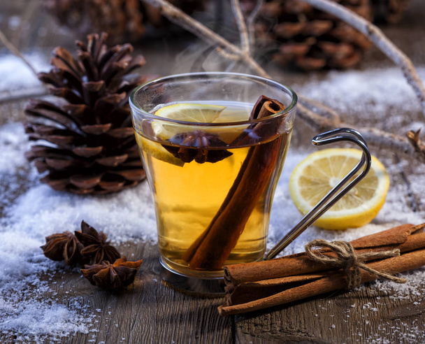 Hot winter beverage with cinnamon, anise and lemon. Winter scene with pine cones and snow. - Фото, изображение
