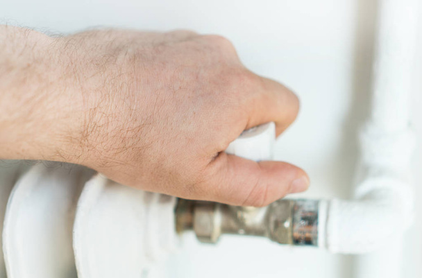 Αρσενική χέρι ρύθμιση θερμοστάτη για να ενεργοποιήσετε τη θερμάστρα καλοριφέρ στο σπίτι. - Φωτογραφία, εικόνα