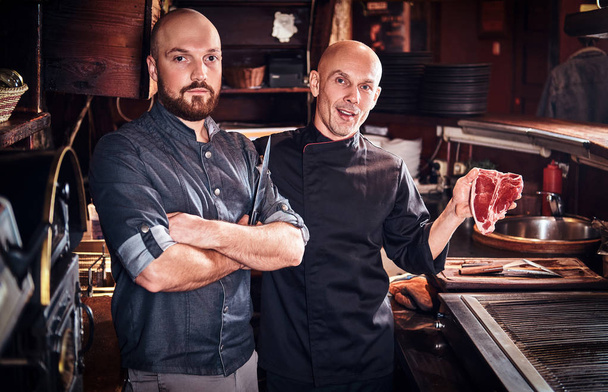 Chef holding a fresh steak and his assistant standing near in a restaurant kitchen. - Photo, Image