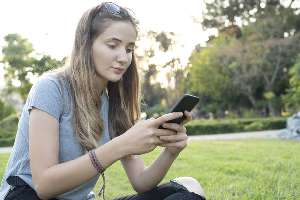 молодая женщина с помощью смартфона в парке. - Фото, изображение