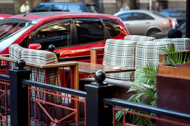 Стол уличного кафе и стулья с мягкими подушками, заведение, огороженное перилами из автомобилей, которые стоят напротив стола
. - Фото, изображение