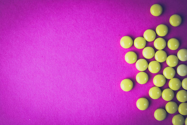 Small yellow orange beautiful medical pharmaceptic round pills, vitamins, drugs, antibiotics on a pink purple background, texture. Concept: medicine, health care. Flat lay, top view - Foto, imagen
