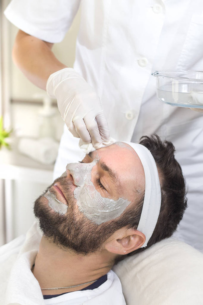 A kezében egy kozmetikus, az egyszer használatos orvosi kesztyűkre mossa a férfi arcát vattatampon - Fotó, kép