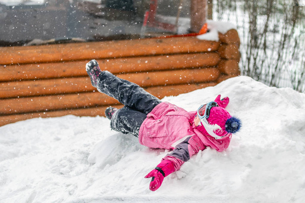 Linda niña en traje deportivo rosa que se divierte jugando al aire libre durante las nevadas en invierno. Niños invierno actividades al aire libre de temporada
. - Foto, Imagen
