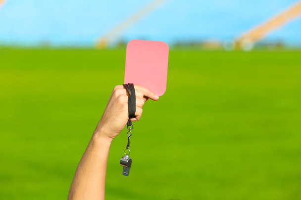 Football referee holding red card and whistle at stadium, closeup - Foto, afbeelding