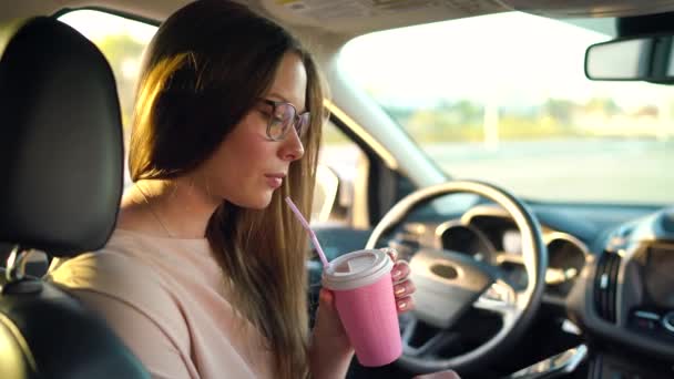 Mujer en gafas habla en el teléfono inteligente y bebe café en el coche
 - Metraje, vídeo