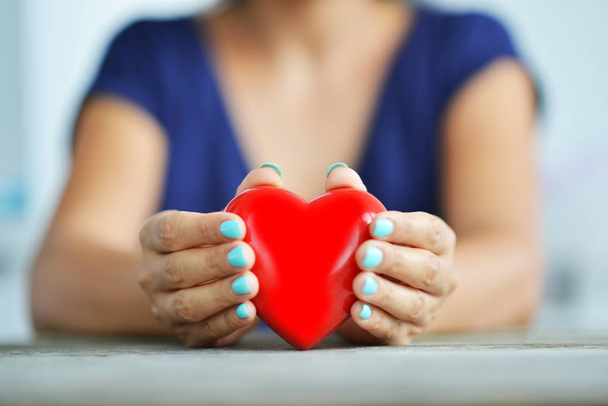 Concepto de salud del corazón con las manos de las mujeres protegiendo un corazón rojo brillante
 - Foto, imagen