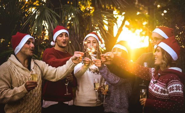Friends-Gruppe mit Weihnachtsmützen feiert Weihnachten mit Champagner-Wein-Toast im Freien - Konzept für tropische Ferien mit jungen Leuten, die die Zeit genießen und gemeinsam Spaß bei Sonnenuntergang haben - Foto, Bild