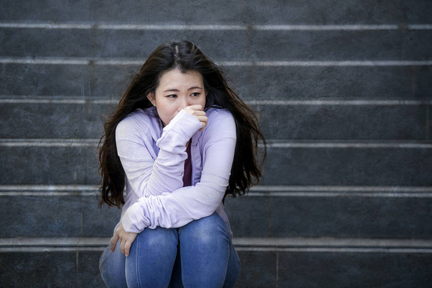 young sad and depressed Asian Chinese student woman or bullied teenager sitting outdoors on street staircase overwhelmed and anxious feeling desperate suffering depression problem  - Фото, изображение