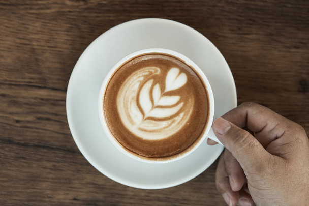 Warme koffie latte beker op houten tafel achtergrond met warme ochtendzon. gelukkig weekend concept. - Foto, afbeelding