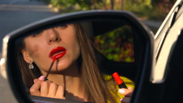 Vrouw schildert haar lippen met lippenstift en kijkt in de achteruitkijkspiegel - Video