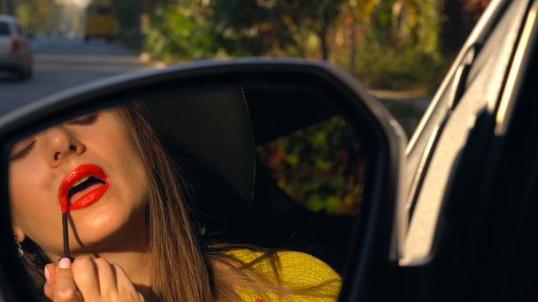 Όμορφη γυναίκα που βάφει τα χείλη με κόκκινο κραγιόν και μοιάζει με το κάτοπτρο οδηγήσεως - Πλάνα, βίντεο