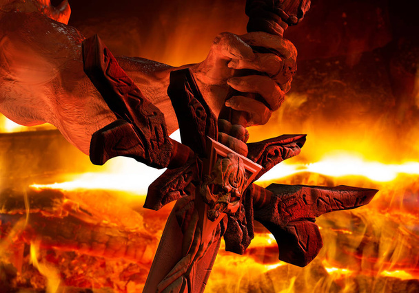 Afbeelding van een hand van de demon met sharped nagels houden een schedel gegraveerde zwaard close-up op brand achtergrond. - Foto, afbeelding