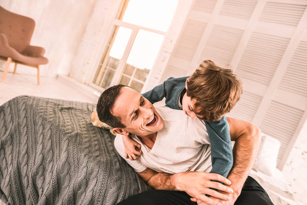 Energetic kid play-wrestling with his dad on the bed. - Fotoğraf, Görsel