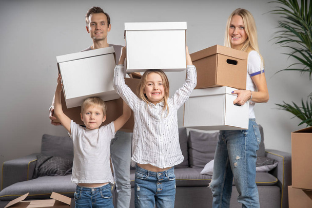 Полнометражное фото счастливой супружеской пары с детьми с картонными коробками в руках стоя
 - Фото, изображение